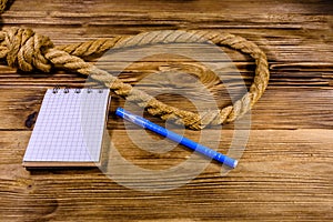 Rope with noose for the suicide, blank notepad and pen on wooden background