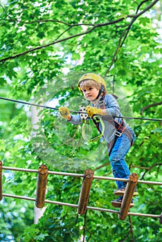 Rope park - climbing center. Carefree childhood. Little child climbing in adventure activity park with helmet and safety