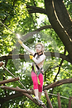 Rope park - climbing center. Happy little girl in summer. Go Ape Adventure. Balance beam and rope bridges. Little girl