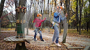 Rope Park. Two little girls in orange helmets in adventure park in safety equipment in autumn day.  Happiness and happy childhood