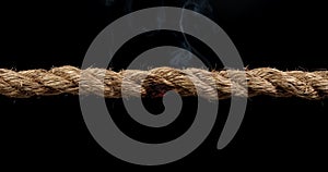 Rope stretched tight and slowly burning apart, finally snapping in two. Concept of dangerous stress or stressful situation like