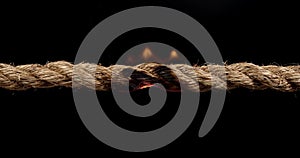 Rope stretched tight and slowly burning apart, finally snapping in two. Concept of dangerous stress or stressful situation like