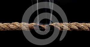 Rope stretched tight and slowly burning apart, finally snapping in two. Concept of dangerous stress or stressful situation like