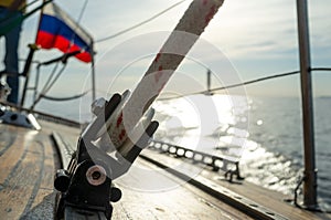 Rope with a winch on a wooden deck of a yacht on a blurred background of a boat on the horizon and the sea, on a summer