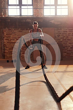 Rope workout. Sport woman doing battle ropes exercise at gym