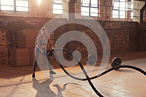 Rope workout. Sport woman doing battle ropes exercise at gym