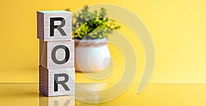 ROR - Rate Of Return. Wooden blocks with the word ROR, yellow bacground. High level of business profitability