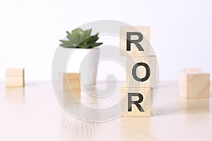 ROR - Rate Of Return. wooden cubes and flower in a pot on background