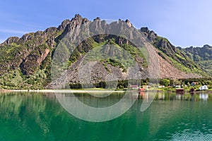 Rorbu fishing huts line a calm fjord in Lofoten, reflecting the majestic mountains