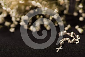 Rosary beads with blurred white small flowers, black background