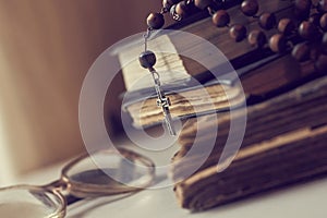 The rosary beads on Catholic Church liturgy books and old glasses on the side of them.