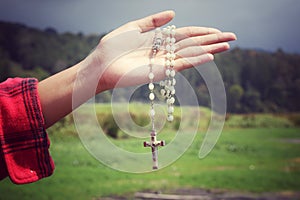 Rosary beads with Jesus Christ holy cross crucifix in young woman hand. Catholic religion symbol.