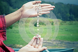 Rosary beads with Jesus Christ holy cross crucifix in young woman hands on green nature background. Catholic religion concept.