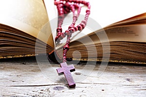 Rosary beads from red wood with cross in an old book on a rusti