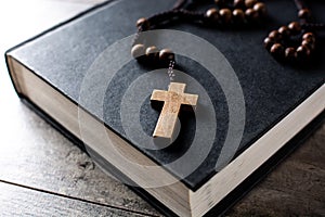 Rosary catholic cross on holy Bible on wooden table photo