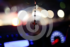 Rosary with cross focused and hanging from center mirror inside the car, rest keeping everything defocused