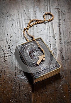 Rosary with cross laying on old Holy Bible book on rustic wooden table.