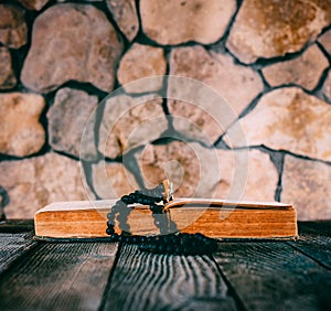 Rosary with a crucifix on an open old book on old wooden table on a background of stone walls