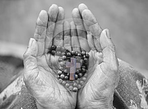 Rosary in hand. Senior woman holding rosary with Jesus Christ holy cross crucifix in hands in black and white background..