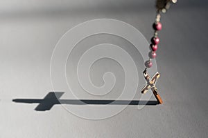 Rosary hanging over white casting cross shadow