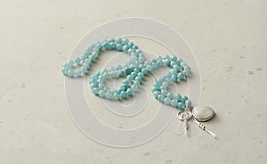 Rosary mala 108 beads from natural stones aquamarine lie on light modern background. Author`s jewelry from natural stones,
