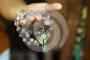 Rosary in one hand. Young junior lady holding rosary with open hand. Female hands holding a rosary with Jesus Christ Cross or
