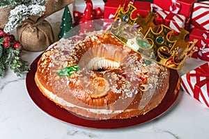 Roscon de reyes with cream and christmas ornaments on a red plate. Kings day concept spanish three kings cake.Typical spanish