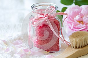 Rose bath salt  in glass bottle, body care accessories and fresh rose petals on light background, spa concept