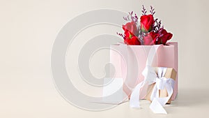 Rose bouquet in paper bag with gift box and card on beige background