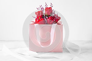 Rose bouquet with pink gift paper bag on white table