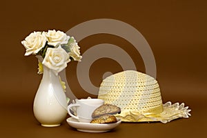 Rose bouquet in a vase, straw hat and coffee with biscotti