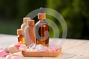 Rose essential oil and flowers on white wooden table outdoors, space for text