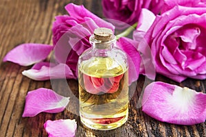 Rose essential oil with pink roses and petals on wooden board