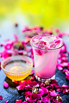 Rose falooda or rose shake in a transparent glass along with some honey in another bowl on wooden surface,Popular summer and