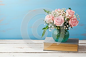 Rose flower bouquet in vase on old books over wooden background