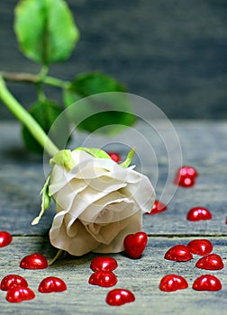 Rose flower and small red hearts scattered on wooden table