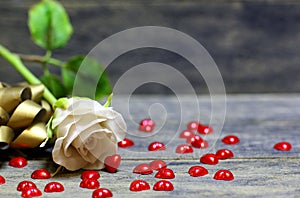 Rose flower and small red hearts scattered on wooden table