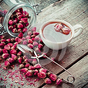 Rose flowers, tea cup, strainer and glass jar with rose buds