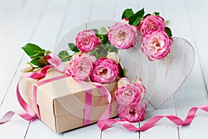 Rose flowers, wooden heart and gift box on blue rustic table. Beautiful greeting card for Birthday, Woman or Mothers Day.