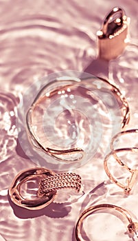 Rose gold bracelets, earrings, rings, jewelery on pink water background, luxury glamour and holiday beauty design for jewelry