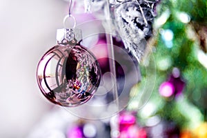 Rose gold pink glass Christmas ball bauble, snowy tree branch, green decoration, white bokeh bg