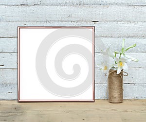 Rose Gold square Frame mockup near a bouquet of lilies stands on a wooden table on a painted white wooden background. Rustic style