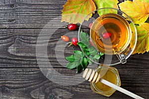 Rose hip tea with honey in transparent cup with autumn leaves