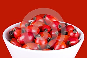 Rose hips in a white bowl over red photo