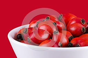 Rose hips in a white bowl on red background photo