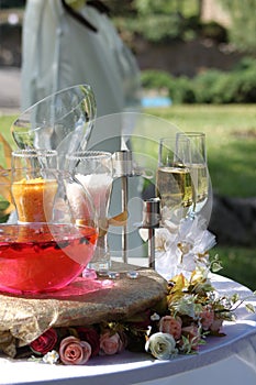 Rose petals float in pink water in a glass spherical vase, white and yellow sand in glasses, two glasses with champagne, decor