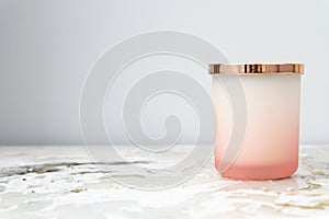 Rose pink and white ombre candle jar with a shiny gold lid, sitting on a bedside table night stand. Candle is not lit. Daytime