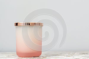 Rose pink and white ombre candle jar with shiny gold lid, sitting on a bedside table night stand. Candle is not lit. Daytime