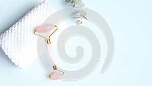 Rose quartz face massage roller with towel and eucalyptus leaf on blue background. Facial massager with jade stone, anti-aging,