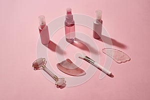 Rose quartz facial massage tools gua sha stone scrapers, face roller and beauty products in plastic bottles isolated on